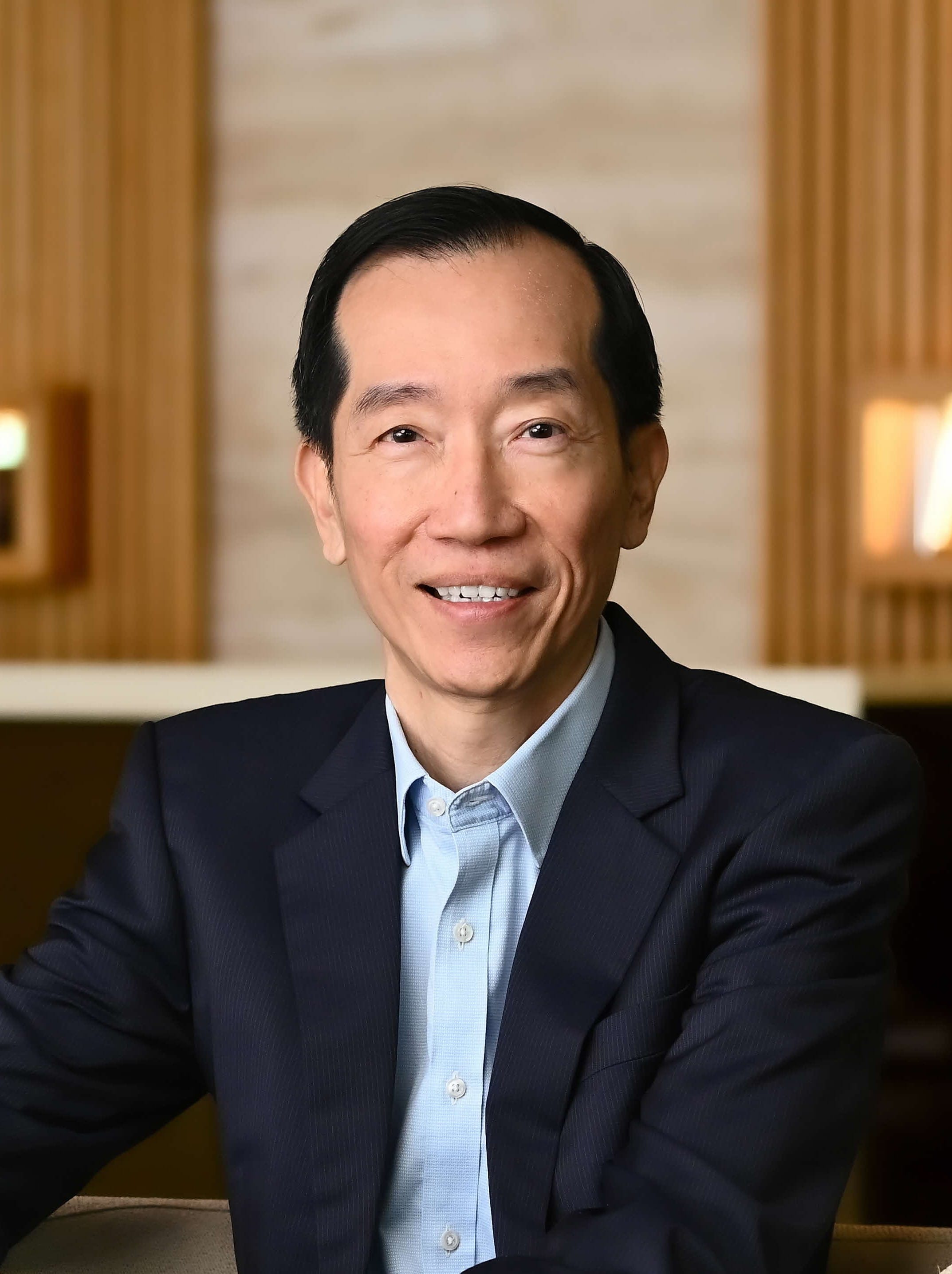 Smiling man in a blue suit with a light blue shirt against a neutral background.